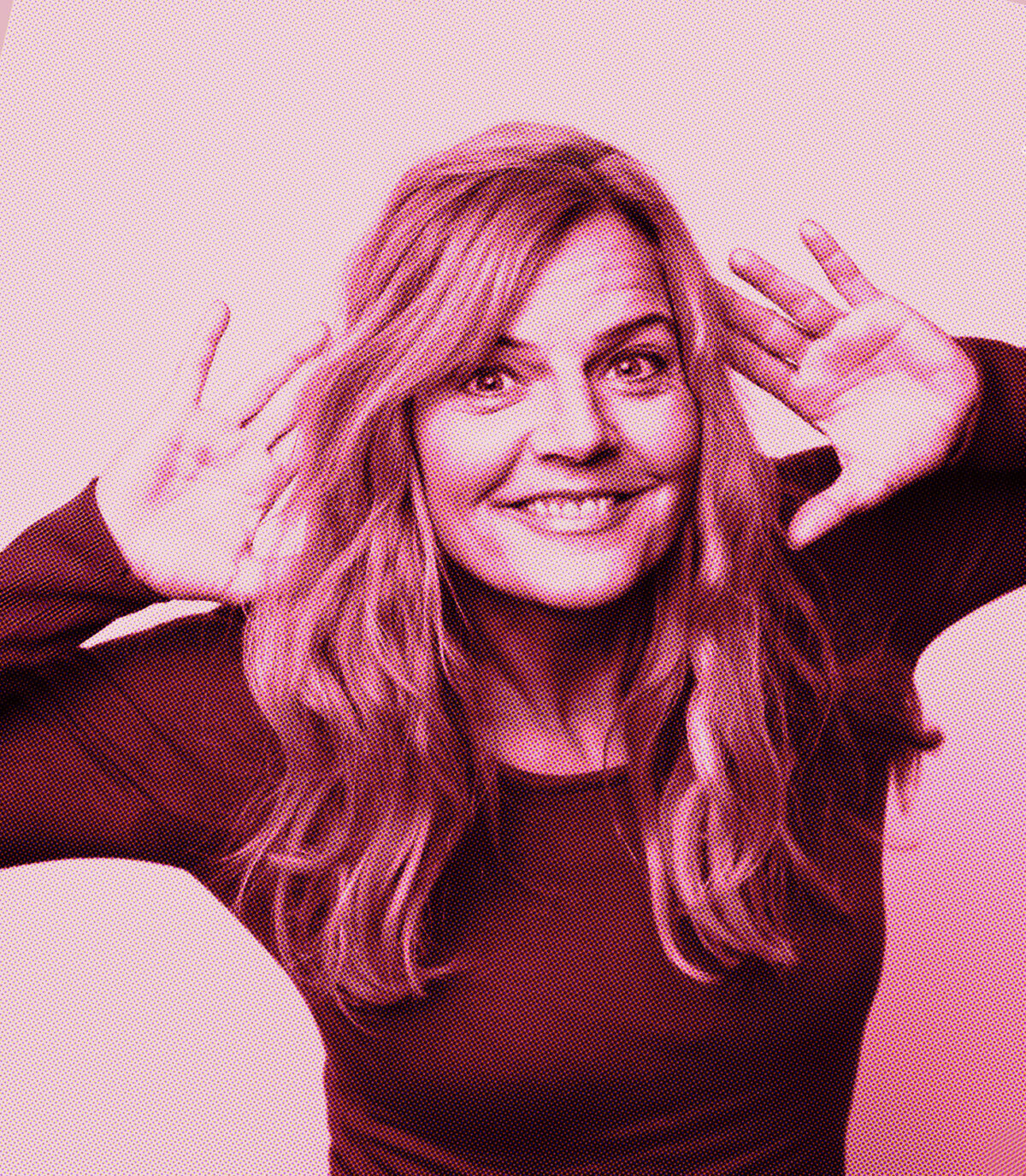 Pink-filtered picture of woman with long hair smiling and holding her hands to the side of her head